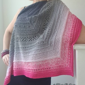 May include: A grey and pink knitted shawl with a lacy pattern. The shawl is draped over a person's shoulders and is made with a gradient yarn that transitions from dark grey to light pink.