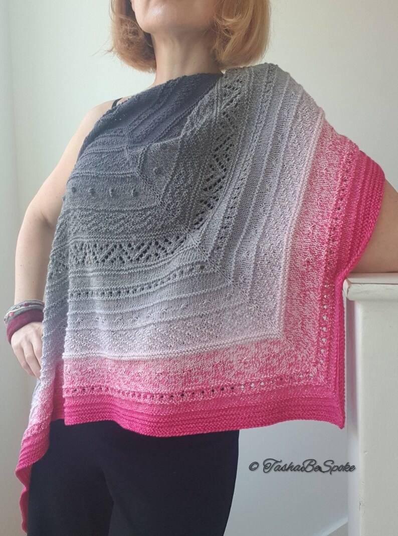 May include: A grey and pink knitted shawl with a lacy pattern. The shawl is draped over a person's shoulders and is made with a gradient yarn that transitions from dark grey to light pink.