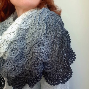 May include: A crocheted shawl with a gradient of colours from white to black. The shawl has a delicate lace pattern and a scalloped edge.