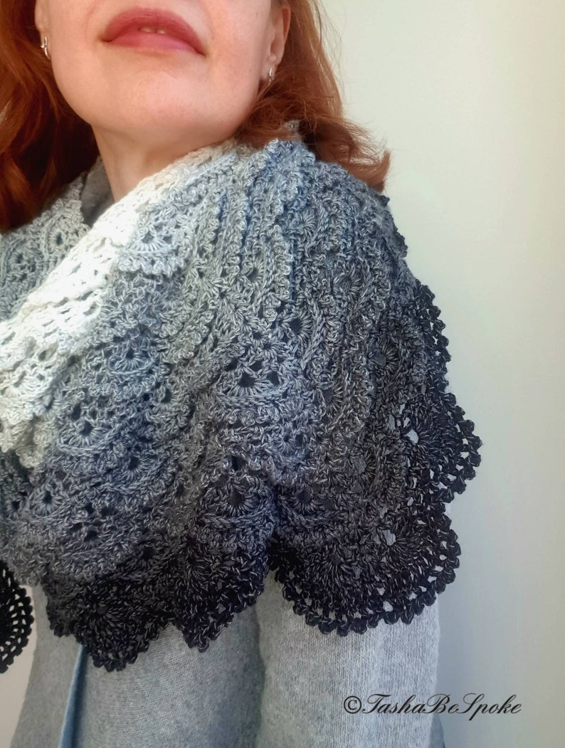 May include: A crocheted shawl with a gradient of colours from white to black. The shawl has a delicate lace pattern and a scalloped edge.