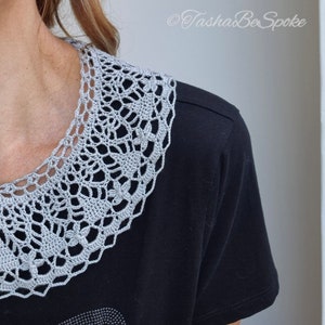 May include: A gray crocheted collar with a delicate floral pattern. The collar is worn over a black t-shirt.