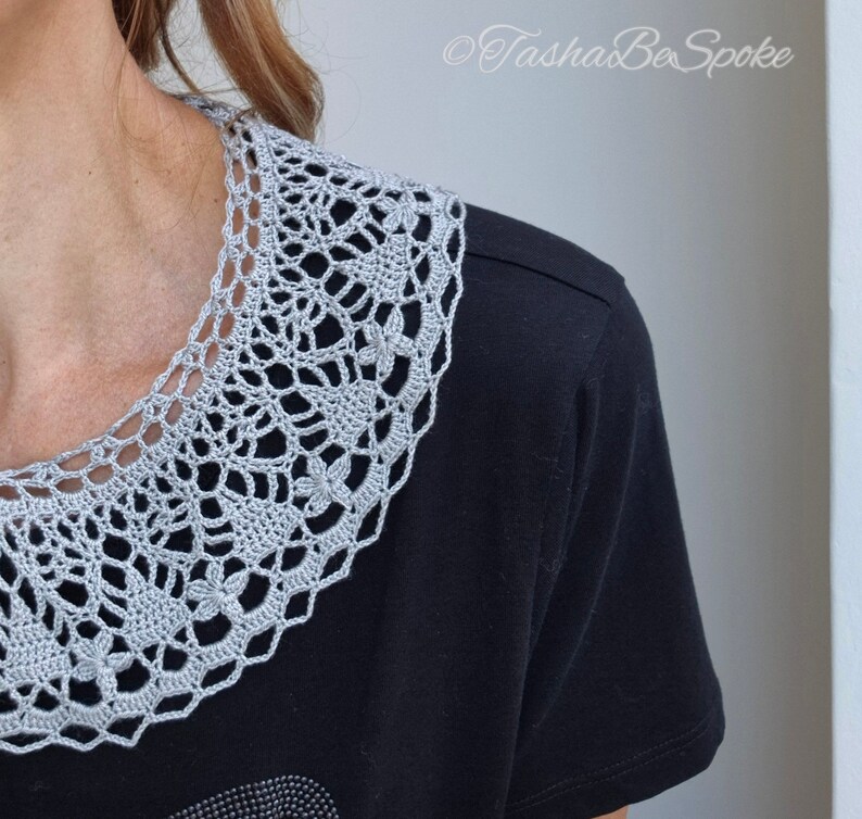 May include: A gray crocheted collar with a delicate floral pattern. The collar is worn over a black t-shirt.
