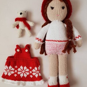 May include: Knitted doll with red hat, white sweater, pink skirt, and red shoes. The doll is holding a white knitted teddy bear wearing a red scarf. The doll also has a red knitted dress with white snowflake pattern.