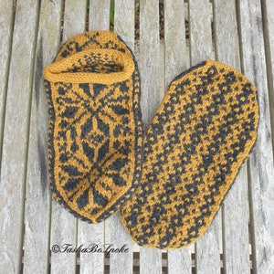 May include: A pair of knitted slippers in a mustard yellow and black color scheme. The slippers have a geometric pattern and are laid out on a wooden surface.