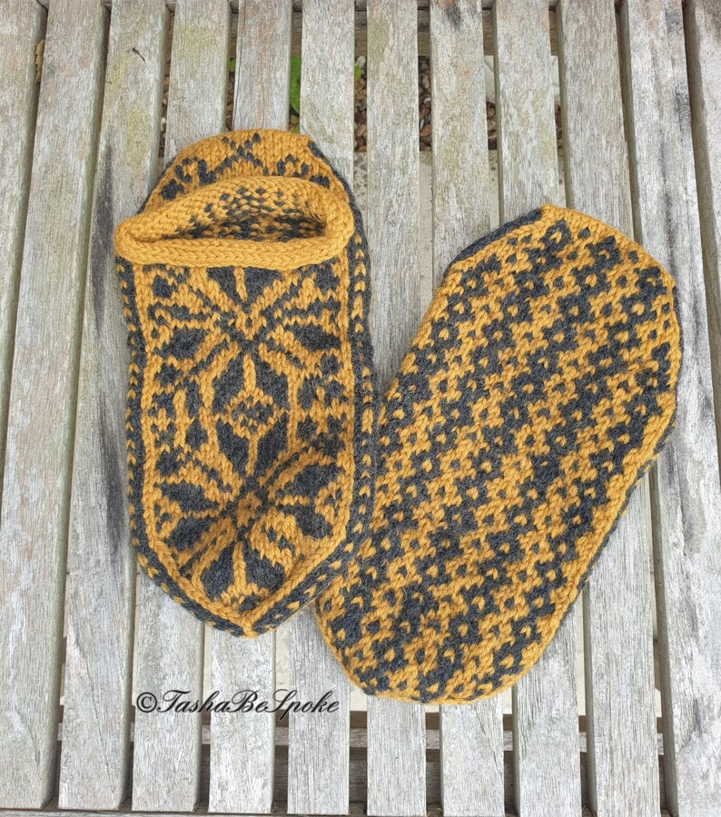 May include: A pair of knitted slippers in a mustard yellow and black color scheme. The slippers have a geometric pattern and are laid out on a wooden surface.
