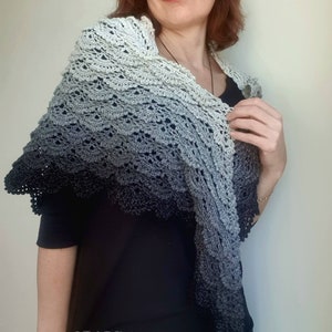 May include: A grey and black ombre crochet shawl with a scalloped edge. The shawl is draped over a person's shoulders.