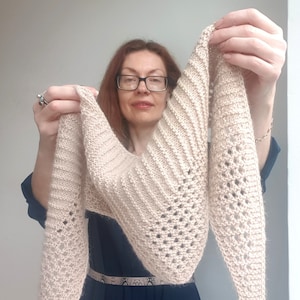 Puede incluir: Un chal de punto beige con un delicado patr&oacute;n de encaje. El chal lo sostiene una persona que lleva un vestido azul oscuro.