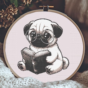 May include: A cross-stitch embroidery hoop featuring a cute pug dog wearing glasses and reading a book. The pug is in black and white, set against a light pink background. The hoop is held in a wooden frame, perfect for home decor.