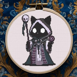 May include: A cross-stitch embroidery in a wooden hoop features a pixelated cat character dressed in a dark robe and hood, holding a staff with a skull and a rose. The design is set against a light background.
