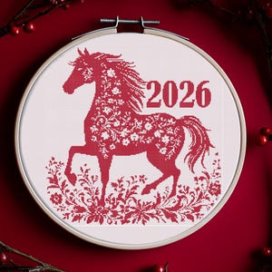 May include: A red cross-stitch embroidery hoop featuring a horse design with floral patterns and the year 2026. The design is set against a white background and surrounded by a red floral wreath.