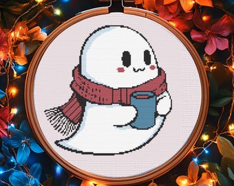 Puede incluir: Un bastidor de bordado de punto de cruz con un simpático fantasma blanco con una bufanda roja y una taza azul. El fantasma tiene mejillas rosadas y una expresión sonriente. El fondo es un arreglo floral con luces de hadas.