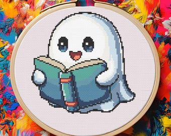 May include: Cross-stitch embroidery of a friendly white ghost reading a teal book. The ghost has blue eyes and a smiling mouth. The embroidery is set in a wooden hoop against a colorful, abstract background.