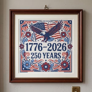 May include: Framed artwork with a patriotic theme. The image features a bald eagle, American flags, and floral designs in red, white, and blue. The text reads "1776-2026 250 YEARS". The artwork is in a brown wooden frame.