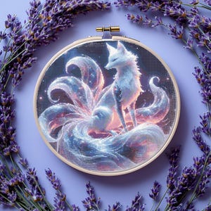 May include: A round embroidery hoop features a white fox with nine tails, rendered in a pixelated style with blue, pink, and purple hues. The fox is set against a dark background with sparkling details. Lavender sprigs frame the hoop on a lavender background.