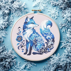 May include: A cross-stitch embroidery hoop featuring a blue fox with intricate floral patterns. The fox is depicted in shades of blue and white, set against a light pink background. The design is framed by a wooden hoop, creating a decorative piece.