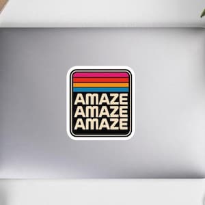 May include: A square sticker with rounded corners featuring a retro-style design. The top section has horizontal stripes in pink, red, orange, and blue. Below the stripes, the word AMAZE is printed in a bold, sans-serif font on three lines.