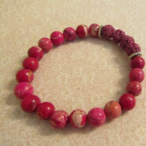 May include: A pink and white gemstone bracelet with a dark pink lava rock bead and silver spacer beads.