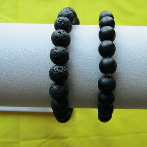 May include: Two black beaded bracelets on a white display stand. One bracelet is made of smooth black beads, the other is made of rough black beads.