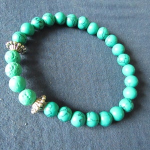 May include: A turquoise beaded bracelet with silver accents. The beads are round and have a textured surface.