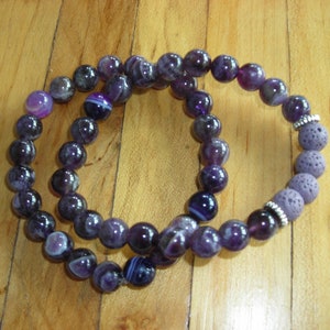 May include: Two amethyst bracelets, one with purple and white striped beads and the other with dark purple beads and lava rock beads.