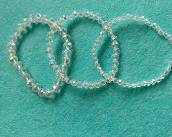 May include: Three clear crystal beaded bracelets on a turquoise background.