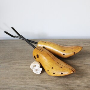 May include: A pair of vintage wooden shoe trees with metal spring mechanisms. The shoe trees are marked "K 47" and "K 48".