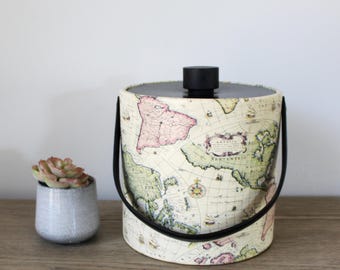 May include: A vintage-style ice bucket with a black lid and handles. The bucket is covered in a map print with a cream background and colorful accents. The map features the continents of North America, South America, Europe, Africa, and Asia.