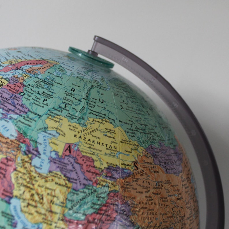 May include: A detailed, colorful globe with political boundaries and geographical features. The globe is mounted on a gray plastic stand. The map shows Eurasia, with a focus on Kazakhstan and surrounding countries. The globe is a tool for education and exploration.