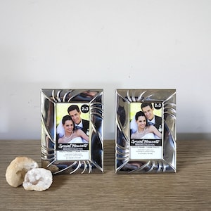 May include: Two rectangular silver-toned metal photo frames with a decorative swirling border pattern. Each frame holds a display card featuring a couple and the text Special Moments Memories Collection Photo Frame 2x3 inches.