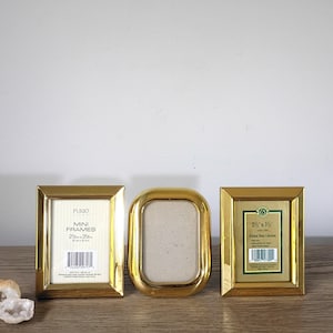 May include: Three polished brass picture frames. Two are rectangular with 2.5 inch by 3.5 inch inserts, and one is oval-shaped. The rectangular frames contain paper inserts with text including "MINI FRAMES" and "Polished Brass Collection".