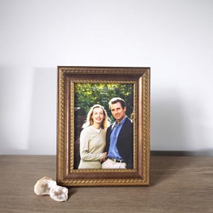 May include: A rectangular picture frame with a metallic bronze finish and a decorative rope-like border pattern. The frame holds a display insert labeled Sonoma Lifestyle 5x7 frame, featuring a photograph of two people standing outdoors.
