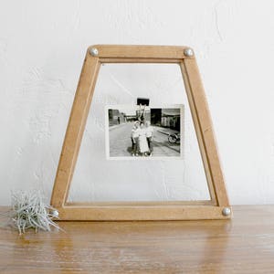 May include: A wooden picture frame shaped like a tennis racket, with a black and white photo of a group of people standing in front of a building. The photo is held in place by a metal clip.