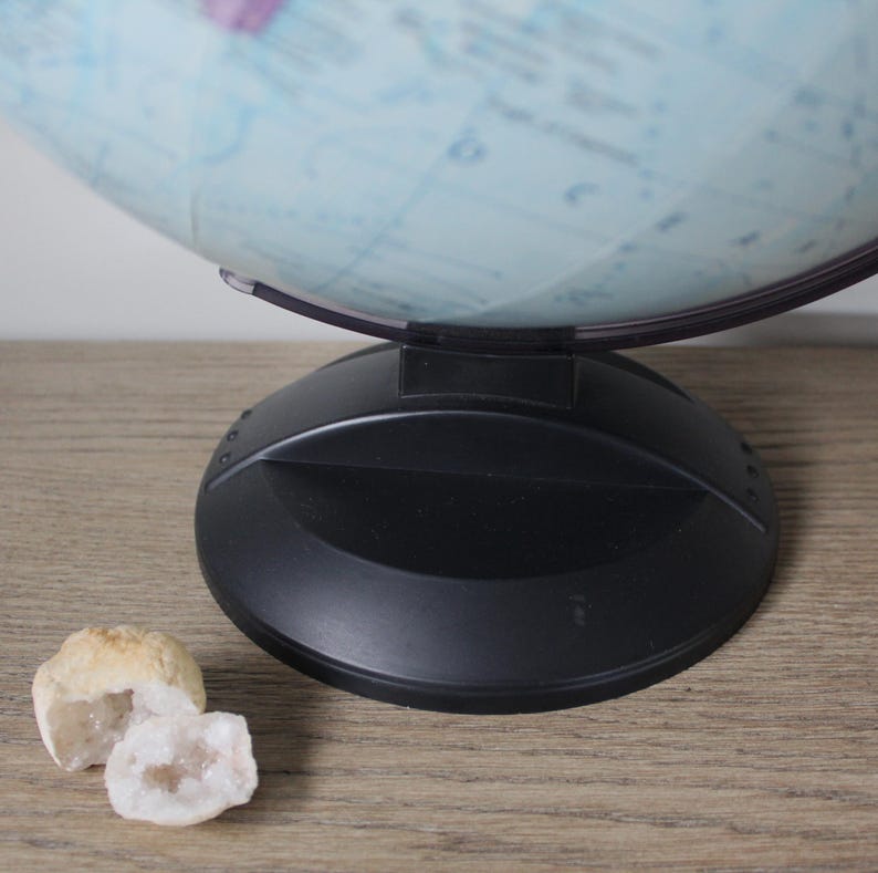 May include: A black globe base supports a light blue and white globe. The globe rests on a wooden surface. Two small, open geodes with crystal formations are in the foreground.