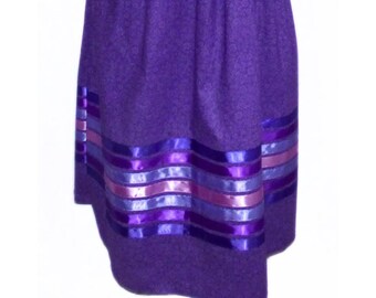 May include: A purple short-sleeved t-shirt paired with a matching purple skirt featuring an elastic waistband and a subtle tonal pattern. The skirt is decorated with five horizontal satin ribbons in shades of purple and lavender.
