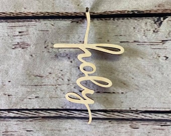 May include: A wooden cutout of the word "holy" in a cursive font. The cutout is light brown and is hanging from a nail on a light wood background.
