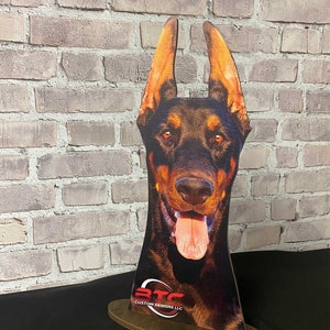 May include: A cutout of a Doberman Pinscher dog's head with a brown and black coat, sticking out its tongue. The cutout is on a wooden base with the text "BTC Custom Designs LLC".