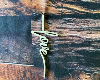 May include: A wooden cross with the word "love" written on it in a cursive font. The cross is a light brown color and is hanging from a string.