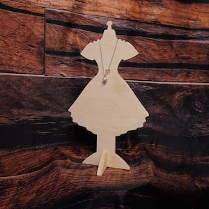 May include: Wooden mannequin shaped like a dress with a silver necklace and a round pendant hanging from it. The mannequin is standing on a wooden base.