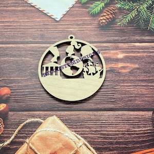 Peut inclure: Ornement de Noël en bois représentant un globe terrestre, un navire, un bâtiment et deux personnages. L'ornement est peint dans des tons de brun et de beige.