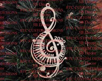 May include: White wooden Christmas ornament shaped like a treble clef with the year 2023 and the word "IAM" inside the clef. The ornament is hanging on a green Christmas tree.