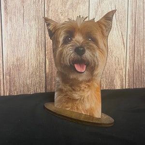 Peut inclure: Une découpe en bois d'un chien brun et beige avec une expression joyeuse. La tête et le cou du chien sont visibles, et la découpe est montée sur une base en bois.