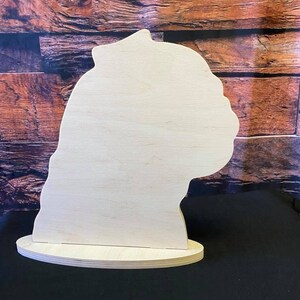 May include: A wooden cutout of a dog's head, with a base. The cutout is unpainted and ready to be decorated.