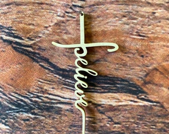May include: A wooden cross with the word "believe" written in cursive on it. The cross is a light brown color and is hanging on a wooden background.
