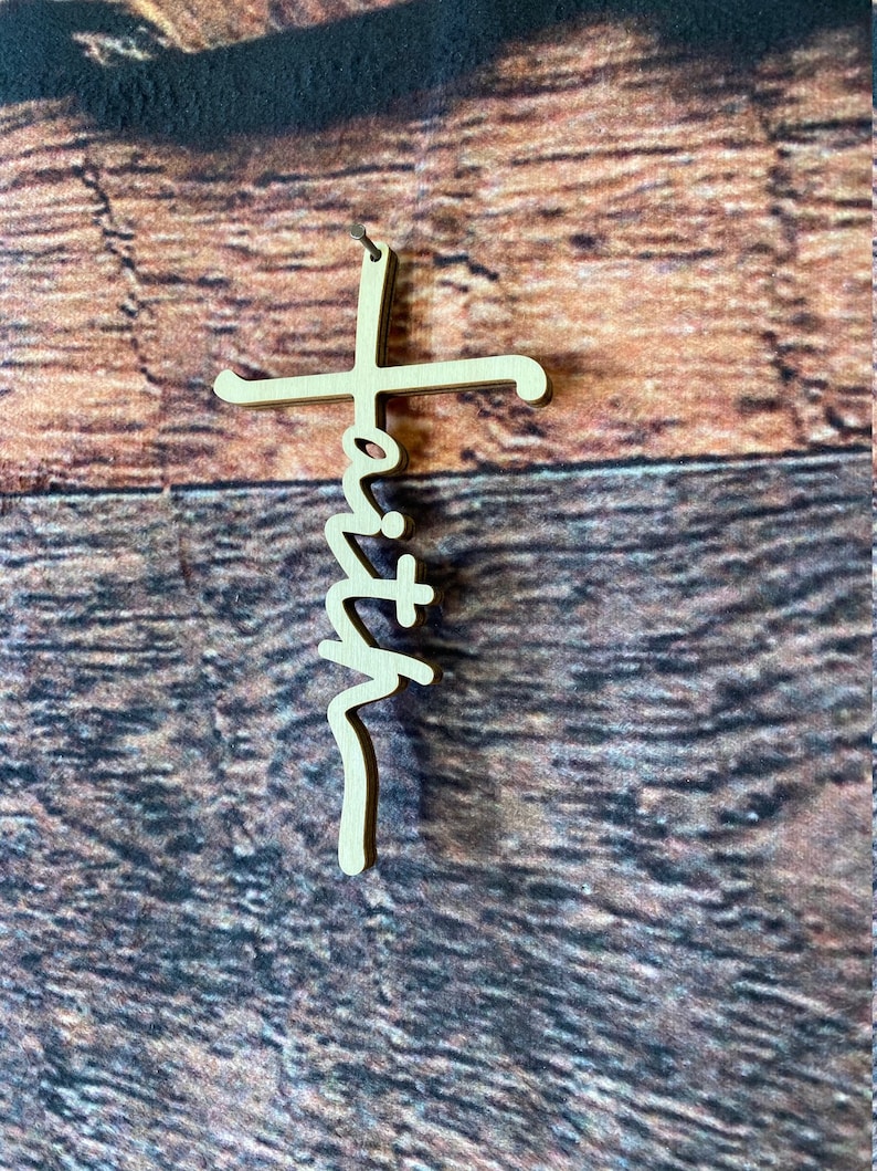 K&ouml;nnte beinhalten: Ein Holzkreuz mit dem Wort "Glaube" in einer stilisierten Schrift.