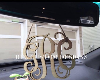 May include: A wooden monogram car charm with the letters "RC" in a cursive font. The charm is hanging from the rearview mirror of a car. The text "BTC CUSTOM DESIGNS" is visible in the image.