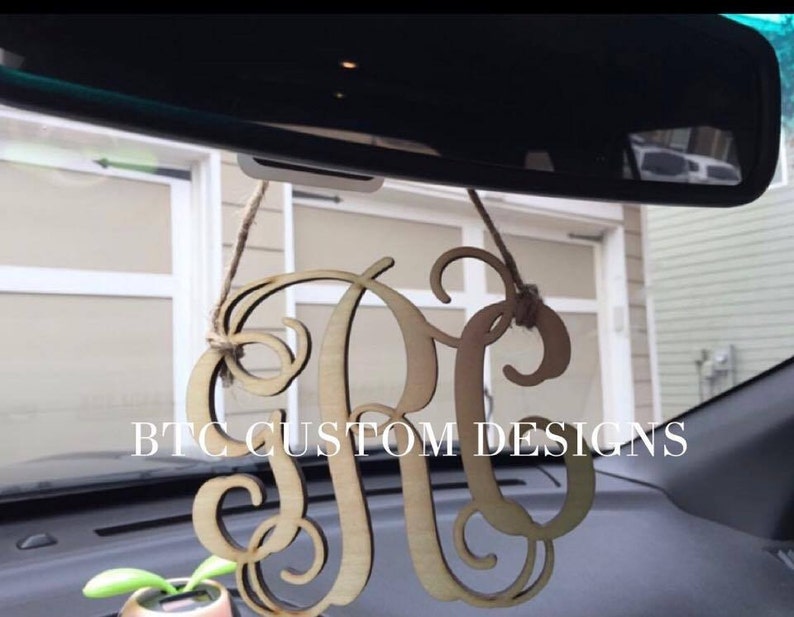 May include: A wooden monogram car charm with the letters "RC" in a cursive font. The charm is hanging from the rearview mirror of a car. The text "BTC CUSTOM DESIGNS" is visible in the image.