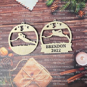 May include: Two wooden ornaments shaped like circles with a person in a skiing pose. The ornament on the right has the text "BRENDON 2022" on it.