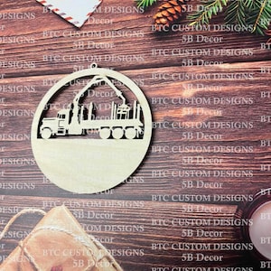 May include: A wooden ornament shaped like a circle with a cutout design of a logging truck with a crane and logs. The ornament is unfinished and ready to be painted or stained.