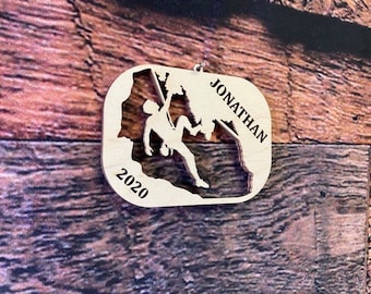 Könnte beinhalten: Ein Holz-Anhänger mit der Silhouette einer Person beim Klettern, dem Jahr 2020 und dem Namen Jonathan.