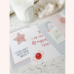 Puede incluir: Cuatro tarjetas de afirmaci&oacute;n con colores pastel e ilustraciones. Las tarjetas muestran el texto "Puedo pedir ayuda cuando la necesito", "Estoy orgulloso de m&iacute; mismo hoy", "Soy valiente" y una estrella de mar rosa con una cara feliz.